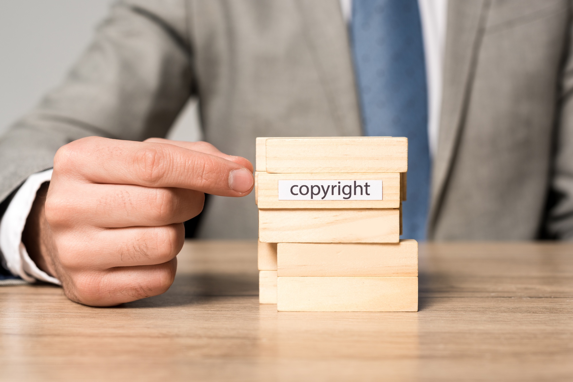 partial view of businessman near blocks wood tower game with copyright inscription isolated on grey